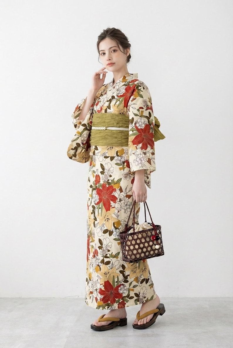 K&ouml;nnte beinhalten: Cremefarbener Kimono mit einem Blumenmuster aus roten und gelben Bl&uuml;ten. Der Kimono ist mit einem gr&uuml;nen Obi-G&uuml;rtel gebunden. Die Person h&auml;lt eine braune gewebte Handtasche und tr&auml;gt Holzsandalen.