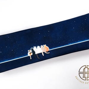 Puede incluir: Una tela azul oscuro con una línea blanca en el medio. Cinco gatos blancos, negros y naranjas están sentados en la línea, mirando hacia el cielo nocturno estrellado.