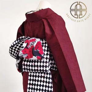 Puede incluir: Kimono burdeos con obi con estampado de rombos en blanco y negro. El obi presenta un diseño floral y de cuervo con rosas rojas. El kimono tiene el texto "ANOTHER DATE NIGHT" en un emblema dorado.