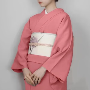 May include: A pink kimono with a white obi featuring a floral design. The kimono is made of a soft, flowing fabric and has a traditional Japanese style.