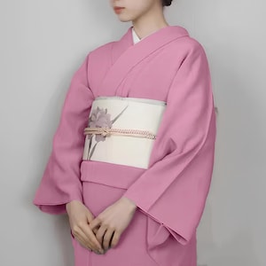 May include: A pink kimono with a white obi featuring a floral design. The kimono has long sleeves and a traditional style.