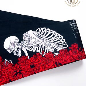 Puede incluir: Tela negra con un esqueleto blanco arrastrándose a través de rosas rojas. La tela tiene texto japonés que dice "El lugar de los muertos está al otro lado de la flor."