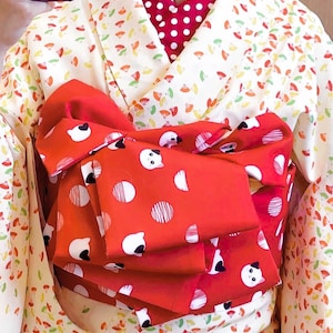 Puede incluir: Un kimono blanco con un cuello rojo de lunares y una faja roja con diseños de osos panda blancos. La faja está atada en un lazo en la parte delantera.
