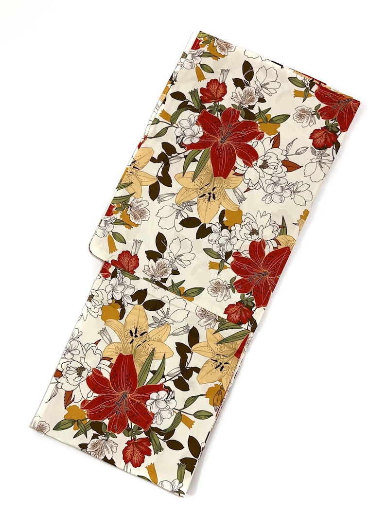 K&ouml;nnte beinhalten: Cremefarbener Stoff mit floralem Muster, das gro&szlig;e rote und gelbe Lilien, wei&szlig;e Bl&uuml;ten und gr&uuml;ne Bl&auml;tter zeigt. Der Stoff ist gefaltet und zeigt das detaillierte Muster. Das Design hat eine Vintage-&Auml;sthetik.