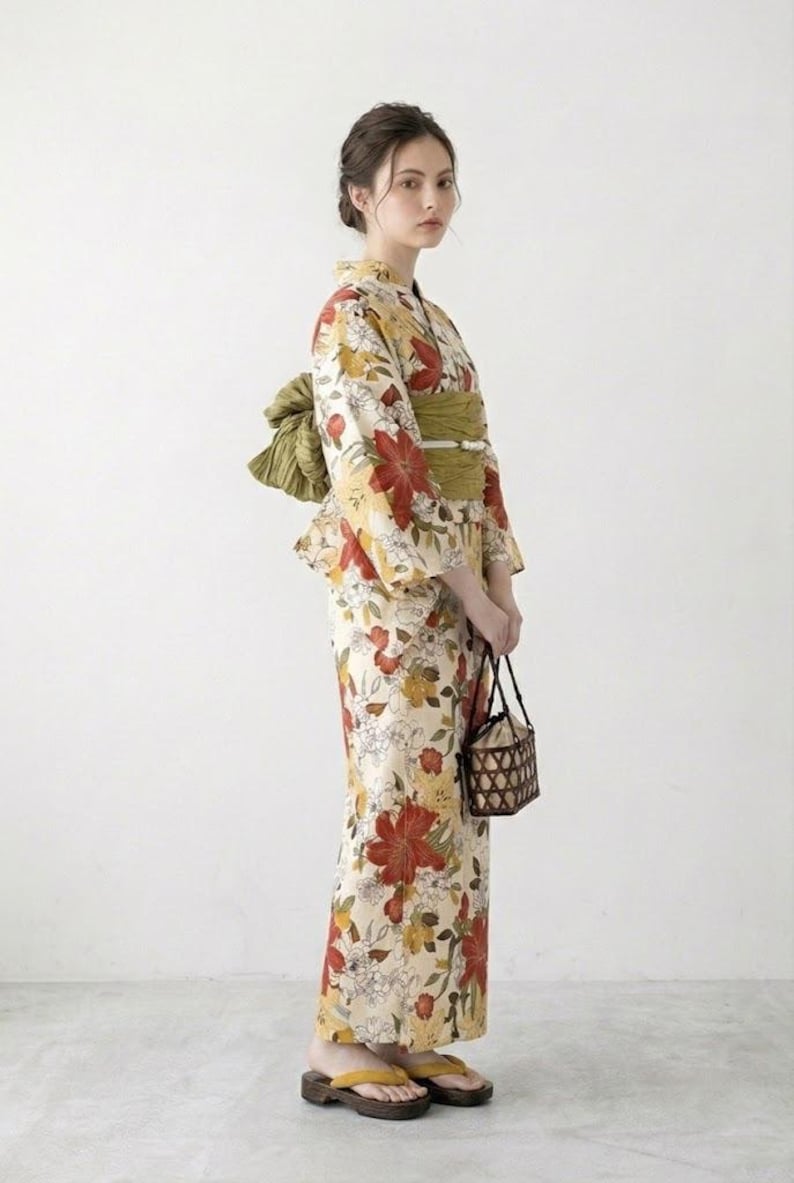 K&ouml;nnte beinhalten: Eine Frau in einem traditionellen japanischen Yukata. Das cremefarbene Kleidungsst&uuml;ck ist mit gro&szlig;en roten und gelben Blumenmustern verziert. Ein gr&uuml;ner Obi-G&uuml;rtel und eine passende Schleife betonen die Taille. Sie tr&auml;gt einen kleinen geflochtenen Korb und Holzsandalen.