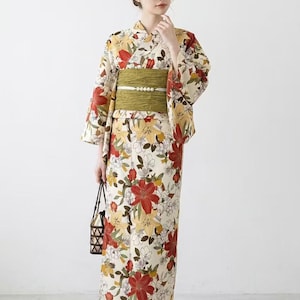 K&ouml;nnte beinhalten: Cremefarbener Kimono mit einem Blumenmuster aus roten und gelben Bl&uuml;ten. Der Kimono wird mit einem gr&uuml;nen Obi-G&uuml;rtel in der Taille zusammengehalten. Die Person tr&auml;gt Holzsandalen und eine kleine schwarze Tasche.