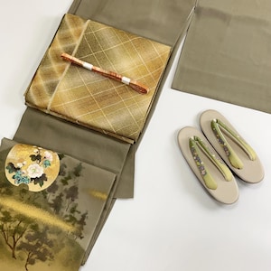 May include: A set of traditional Japanese clothing, including a kimono with a gold and green landscape design, a matching obi with a gold and brown checkered pattern, and a pair of white sandals with green and purple floral embroidery.