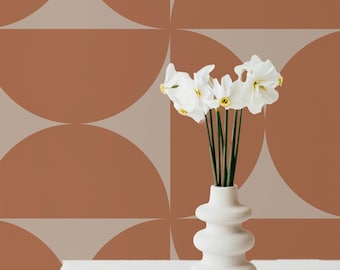 May include: White flowers in a white ceramic vase with a textured surface. The vase is in front of a wall with a geometric pattern of brown and beige semi-circles.