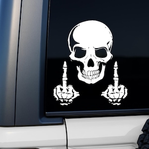 May include: White skull sticker with raised middle fingers. The skull features detailed eye sockets, a nose cavity, and a full set of teeth. The hands are skeletal, with the middle fingers raised. The sticker is on a black background.