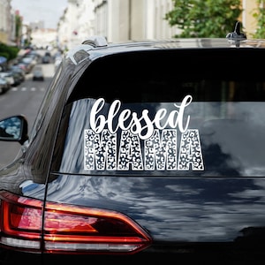 May include: A black car with a white vinyl decal on the back window that says "blessed mama" with a leopard print pattern.
