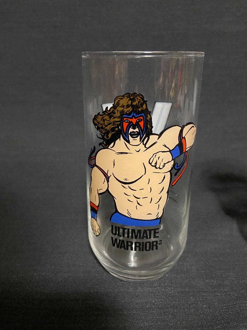 May include: A clear glass with a colorful illustration of a wrestler with the text "ULTIMATE WARRIOR" printed on the bottom.