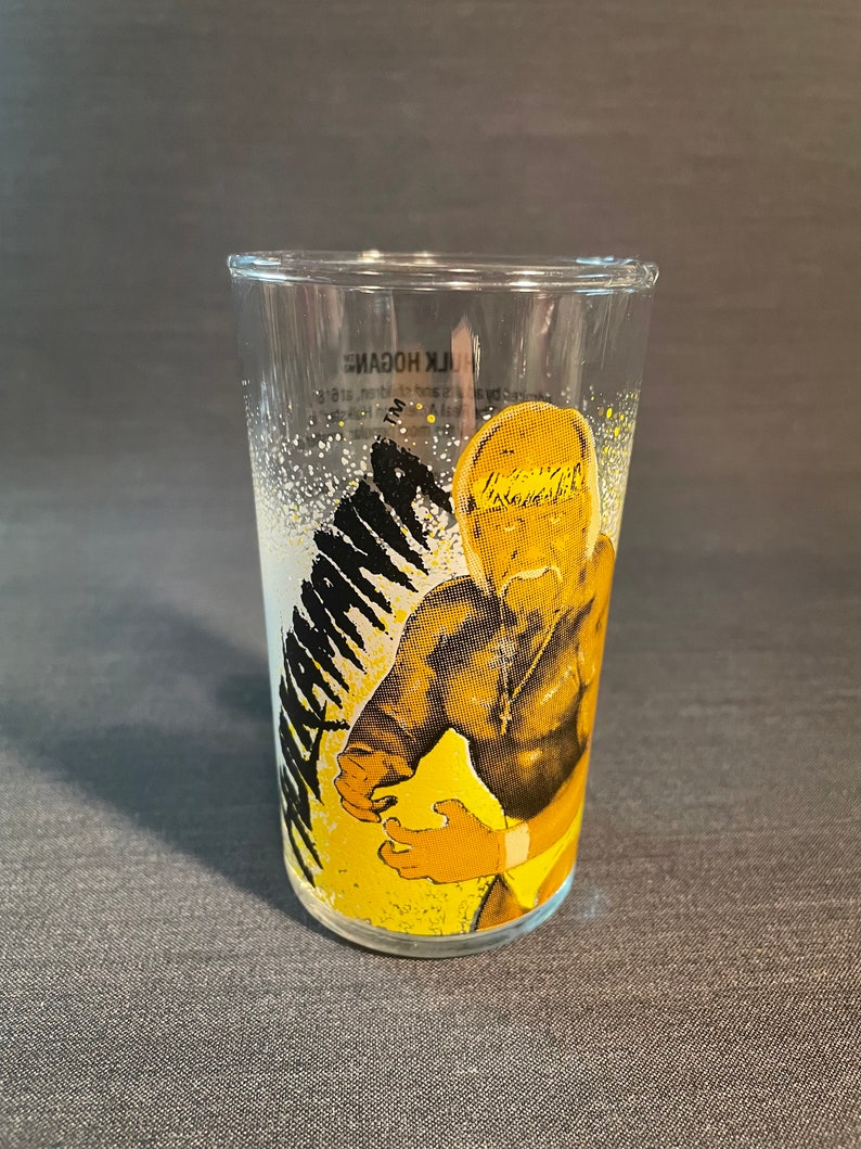 May include: A clear glass with a yellow and black image of Hulk Hogan, a professional wrestler, with the text "Hulk Hogan" on the glass.