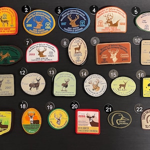 May include: A collection of vintage Deer Hunter patches and a Ducks Unlimited patch. The patches feature deer illustrations, text, and years from 1993 to 2016. Various shapes and colours.