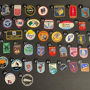 May include: A collection of 50 colourful embroidered patches, featuring various designs, including logos, animals, and text. The patches are arranged in rows on a black background.