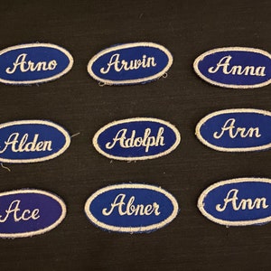 Peut inclure: Douze patchs en tissu ovales de couleur bleue avec des lettres brodées blanches. Les noms sur les patchs sont Arno, Arwin, Anna, Alden, Adolph, Arn, Ace, Abner et Ann.