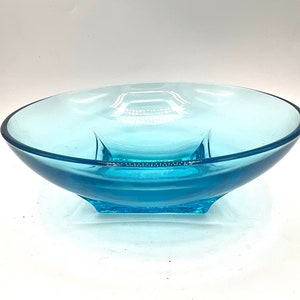 Puede incluir: Un cuenco de vidrio azul claro con una base cuadrada. El cuenco está hecho de vidrio transparente y tiene un acabado ligeramente esmerilado.