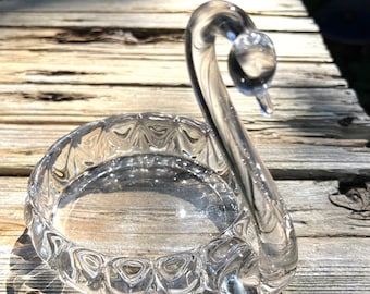 May include: A clear glass swan-shaped trinket dish with a textured, scalloped edge.
