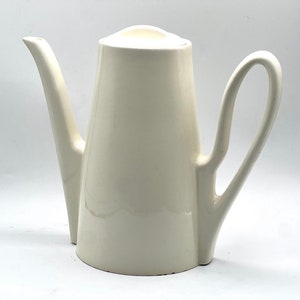 May include: A white ceramic teapot with a tall, slender body and a curved handle. The teapot has a simple, elegant design.