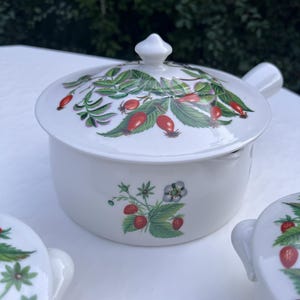 May include: White ceramic casserole dish with a lid. The dish and lid are decorated with a floral pattern of green leaves, red berries, and white flowers.