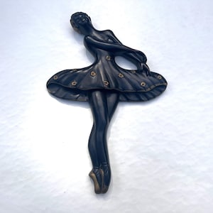 May include: Black ballerina wall decor with gold accents. The ballerina is wearing a black tutu with gold flowers and is posed in a graceful dance position.