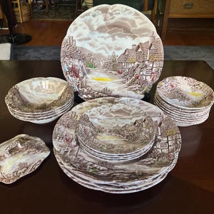 Puede incluir: Un juego de vajilla de cerámica vintage con un diseño de pueblo en tonos marrones y beige. El juego incluye platos grandes, platos más pequeños, cuencos y una fuente. Los platos tienen un borde festoneado. Los platos miden unos 25 cm de diámetro.