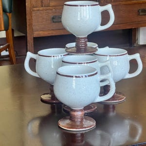 Op de afbeelding: Handgemaakt houten bord met de tekst "Welcome" in een speels lettertype. Het wit geschilderde bord heeft zwarte letters en een bloemmotief. Ontworpen om aan een deur of muur te hangen.