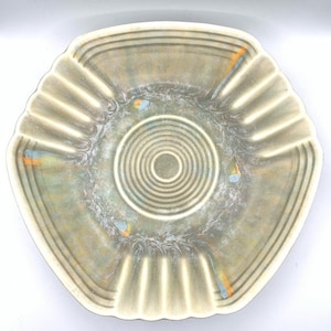 May include: A light green ceramic bowl with a scalloped edge and a concentric circle design in the center. The bowl has a mottled glaze with hints of blue and orange.