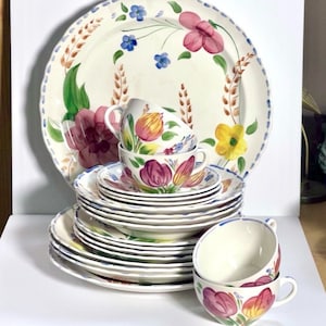 May include: A set of vintage floral patterned china, including a large platter, a stack of dinner plates, and two teacups. The pattern features colorful tulips, leaves, and wheat stalks on a white background.