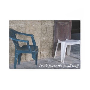 Puede incluir: Una silla de plástico azul y un taburete de plástico blanco se encuentran frente a una pared de ladrillo. El texto "Don't sweat the small stuff" está escrito debajo de las sillas.