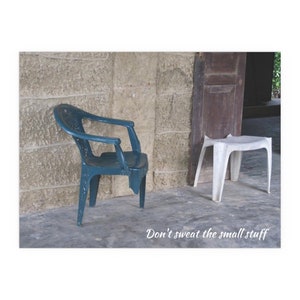 Può includere: Una sedia di plastica blu turchese si trova accanto a uno sgabello di plastica bianco davanti a un muro di pietra. Il testo "Don't sweat the small stuff" è scritto sotto le sedie.