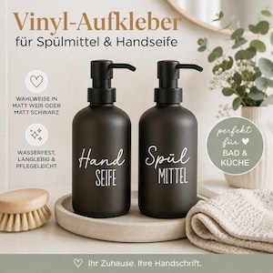Könnte beinhalten: Zwei schwarze Seifenspender mit weißen Etiketten mit der Aufschrift "Hand Seife" und "Spül Mittel". Die Spender haben schwarze Pumpköpfe und stehen auf einem hellgrauen Tablett. Der Text oben lautet "Vinyl-Aufkleber für Spülmittel & Handseife".