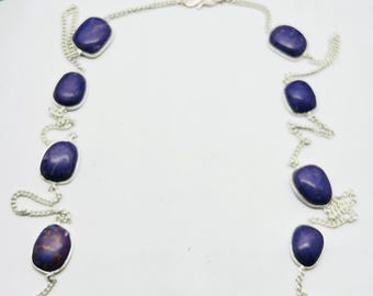 May include: A silver chain necklace featuring oval, dark blue gemstones. The gemstones are evenly spaced along the chain, with a simple clasp closure. The necklace is displayed on a white background.