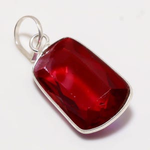 Puede incluir: Un colgante de piedra roja con una argolla de plata. La piedra preciosa es facetada y tiene una forma rectangular.