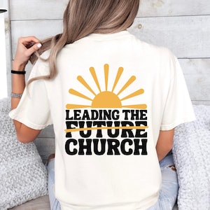 May include: A white t-shirt with a black graphic of a sun and the text "LEADING THE FUTURE CHURCH" with the word "FUTURE" crossed out.