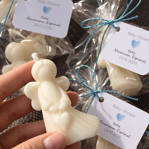 K&ouml;nnte beinhalten: Eine wei&szlig;e engelf&ouml;rmige Kerze mit einem kleinen Herz in den H&auml;nden. Jede Kerze ist einzeln in Klarsichtfolie verpackt, mit blauem Garn verschn&uuml;rt und mit einem wei&szlig;en Etikett versehen, das Baby-Shower, ein blaues Herz, Baby Neumann Espinal und 09.10.2026 zeigt.