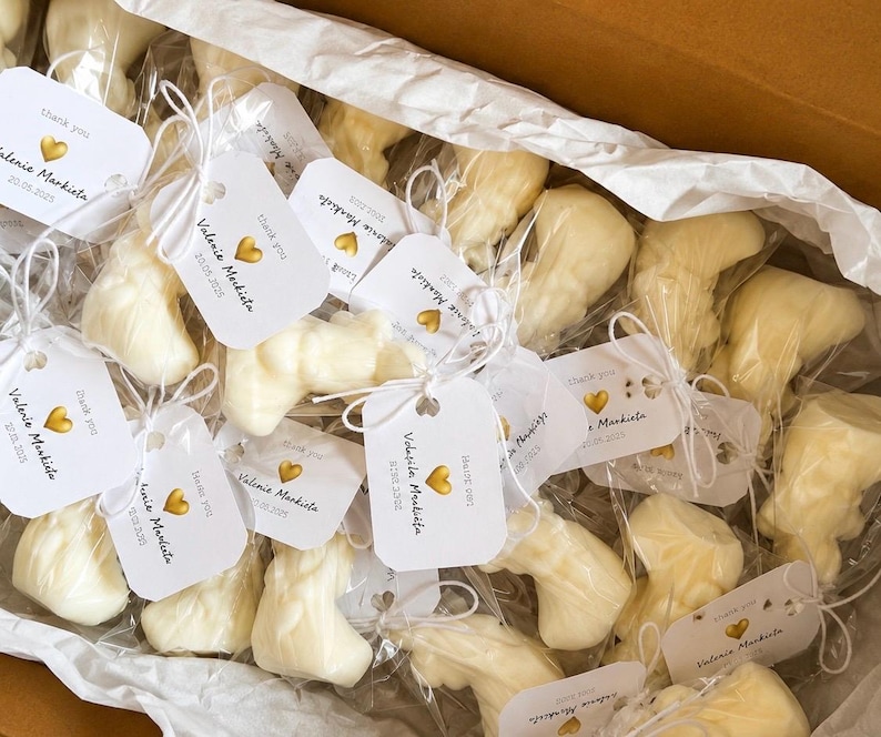 K&ouml;nnte beinhalten: Eine Sammlung einzeln verpackter, wei&szlig;er, stiefelf&ouml;rmiger Objekte in einer Schachtel. Jeder Artikel ist mit einer wei&szlig;en Schnur an einem wei&szlig;en Etikett befestigt, das ein goldenes Herzsymbol, den Text 'thank you', den Namen 'Valerie Markieta' und das Datum '20.05.2025' zeigt.