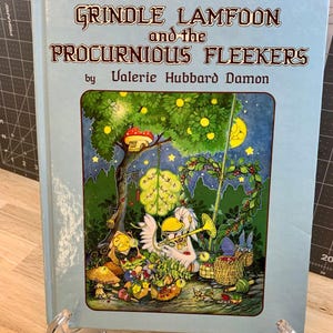 May include: A vintage children's book titled "Grindle Lamfoon and the Procurious Fleekers" by Valerie Hubbard Damon. The cover features a whimsical illustration with a tree, moon, and various cartoon characters in a colorful scene.