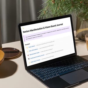 May include: A laptop displaying a "Notion Manifestation & Vision Board Journal" page. The screen shows text about intention and alignment. A wooden bowl with granola, a glass of tea, and a candle holder are also on the table.
