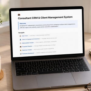 May include: A laptop displays a "Consultant CRM & Client Management System" interface. A cup of coffee, a small potted plant, a notepad, a pen, and eyeglasses are on the wooden desk. The screen text includes "Client & Engagement Database" and "Revenue Tracker."