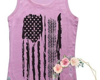May include: A pink tank top featuring a black distressed American flag design. The flag is made up of white stars and black stripes. The tank top has a scoop neck and thin straps.