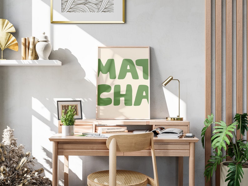 May include: A light wood desk with a green and white poster that says "MATCHA" on it. There is a gold lamp, a potted plant, and a chair with a woven seat.