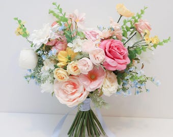 May include: A floral bouquet featuring a mix of artificial flowers in shades of pink, white, yellow, and light blue. The arrangement includes large roses, smaller buds, and green foliage, all tied together at the base with a light blue ribbon.