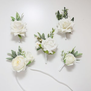 May include: Five white rose boutonnieres with greenery, perfect for a wedding or special event.