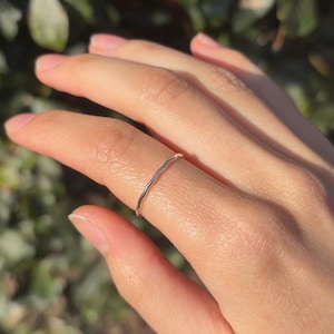 May include: A thin, silver, wavy ring worn on a finger.