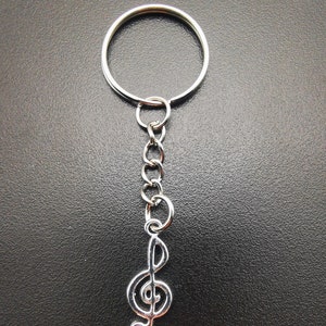 Könnte beinhalten: Ein silberner Schlüsselanhänger mit einem Charm in Form eines Violinschlüssels. Die Kette ist an einem silbernen Schlüsselring befestigt.