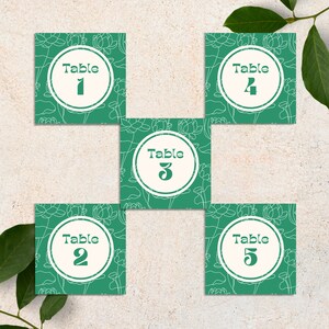 May include: Five green table number cards with white floral designs and white circles with the text "Table" and a number from 1 to 5.