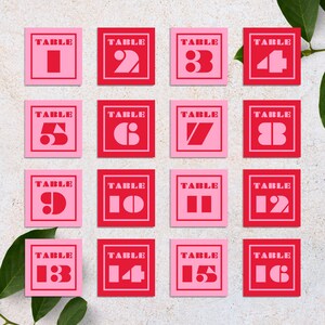 May include: A set of 16 pink and red table number cards with white text. The cards are numbered 1 through 16. The cards are arranged in a grid pattern.