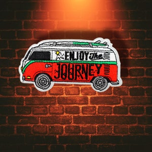 May include: Embroidered patch featuring a red, white, and green van with the text "ENJOY THE JOURNEY." The van has surfboards on top and a mountain and sun graphic. The patch is bordered in white and has a retro design.
