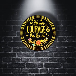 May include: A black and gold embroidered patch with the text "Have Courage & be kind" surrounded by a floral design.
