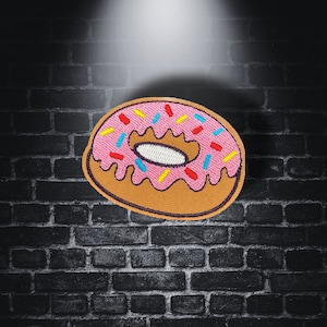 May include: A pink and brown embroidered donut with colorful sprinkles. The donut is on a black brick background.